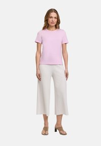 Helles rosa Kurzarm-T-Shirt aus weichem Stoff, kombiniert mit weißen gerippten Schlaghosen und beigen Sandalen mit offenen Zehen.