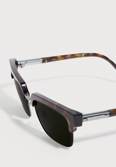 Γυαλιά ηλίου σε σχέδιο κελύφους χελώνας με σκοτεινούς ορθογώνιους φακούς και ασημένιους μεταλλικούς βραχίονες με εγχάρακτο το λογότυπο Dolce & Gabbana, παρουσιάζονται σε γωνία πάνω σε λευκή επιφάνεια.