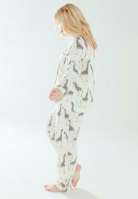 Set di pigiama bianco con motivo di giraffe nere, caratterizzato da maniche lunghe, chiusura con bottoni e rifiniture arancioni a contrasto sui polsini e sui pantaloni.