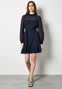 Vestido azul marino con cintura ajustada, mangas largas de viso y detalle de cuello con lentejuelas. Tela suave con falda acampanada.