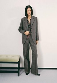 Traje gris a medida con un acabado texturizado, que incluye un blazer de un solo botón, un chaleco de doble botonadura y pantalones de pierna ancha.