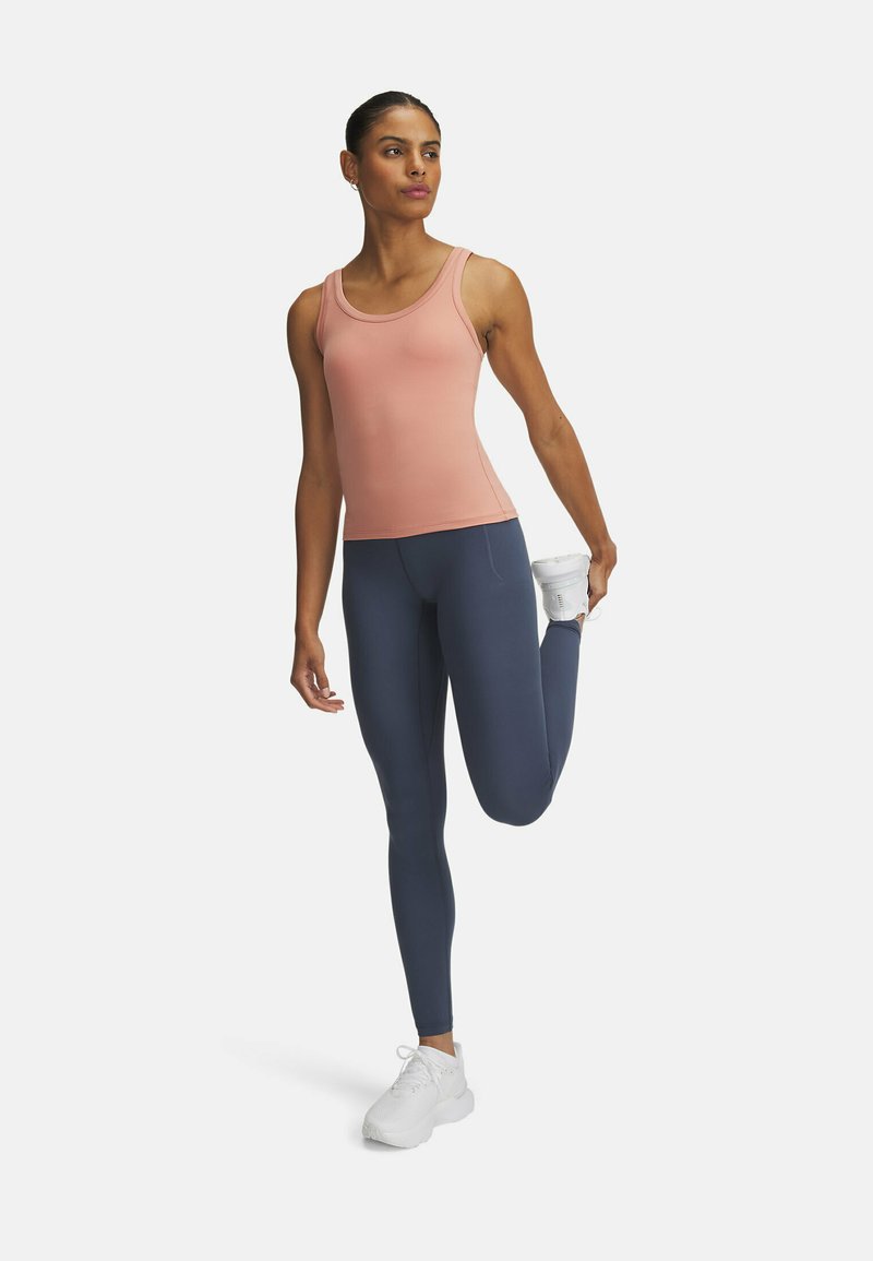Top da donna senza maniche di color rosa chiaro, leggins elasticizzati blu navy e scarpe da ginnastica bianche. La modella sta eseguendo uno stiramento delle gambe, con un aspetto morbido e aderente.