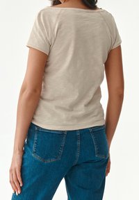 Camiseta de manga corta beige con un ajuste relajado y costuras visibles, combinada con unos vaqueros de denim azul con bolsillos traseros.