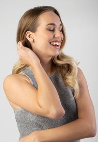 Grijze mouwloze gebreide top met metallic draden, ronde halslijn en een textuurpatroon. Model heeft lang blond haar en een lichte huid.