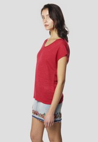 Červené tričko s krátkym rukávom a výstrihom do V, vyrobené z mäkkej, textúrovanej tkaniny. Kombinované s rifľovou sukňou zdobenou farebnou kvetinovou výšivkou na leme.