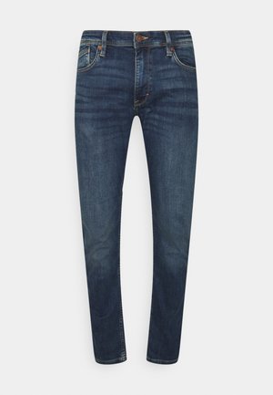 Jean slim bleu foncé avec fermeture à bouton et fermeture éclair à l'avant, cinq poches et légère décoloration sur les cuisses et les genoux.