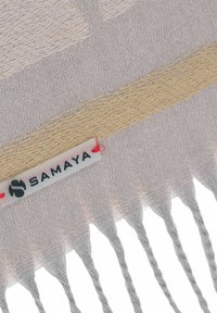 Beige and gray scarf featuring textured fabric, fringe edges, and a white label with "SAMAYA" printed in black.