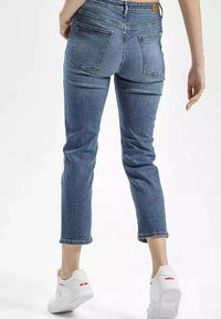 Slim-fit, średnio-wysokie niebieskie dżinsy z tylnymi kieszeniami, postrzępionym dołem i lekkim strechem. Połączone z białymi trampkami z czerwonymi akcentami.
