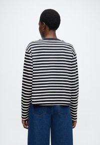 Cămașă cu mâneci lungi, cu dungi în nuanțe de bleumarin și crem, realizată dintr-un material moale; croială lejeră cu tiv drept, asortată cu pantaloni din denim cu picioare largi.