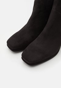Bottines en daim noir avec un bout carré, présentant une texture lisse et une fermeture éclair latérale pour un enfilage facile.