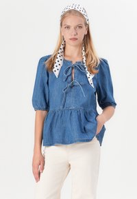 Denim peplum top s nafúkanými rukávmi, detailom mašle na výstrihu a svetlomodrou farbou. V kombinácii s off-white nohavicami. Šatka s bodkovaným vzorom.