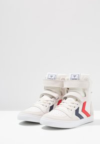 Vita högskor av mocka och tyg, med röda och marinblå ränder, snörning framtill och kardborreband vid vristen.