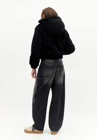 Black fleece hoodie with a hood, cropped design, paired with high-waisted dark gray wide-leg jeans featuring pockets. Light-colored sneakers.