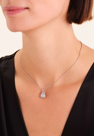 Collana in argento con pendente a goccia caratterizzato da un design testurizzato e dettagli scintillanti, indossata su un tessuto scuro.