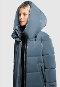 Täpne sinine jakk suure kapuutsiga. Omab läikivat viimistlust, nupuvajutusi ja tõmbluku küljetaskut. Pehme tekstuur, kaasaegne disain.