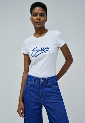 Camiseta blanca con el logo bordado en azul de "Salsa Jeans", diseño ajustado, mangas cortas, combinada con pantalones de mezclilla azules de cintura alta.