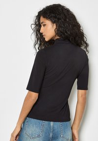 Top nero a maniche corte con collo alto, design aderente e texture liscia, abbinato a jeans di jeans azzurri a vita alta.