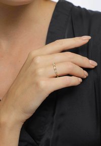 Bague en or avec des pierres rectangulaires serties dans une fine bande. Une main repose sur un vêtement noir, mettant en valeur le design et les détails de la bague.