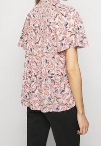 Krátký rukáv, růžová květinová blůza s volánovým designem a nařasením na zadní straně. Obsahuje vzor oranžových a modrých květin na lehkém materiálu.