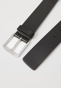 Melns ādas jostas ar elegantu sudraba metāla sprādzi. Jostas virsma ir gluda, un tā ir taisna, ar caurumiem regulēšanai.