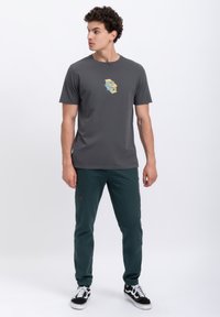 Grijze korte mouwen t-shirt met een geometrische grafiek aan de voorkant, gecombineerd met donkergroene joggers en zwarte sneakers.