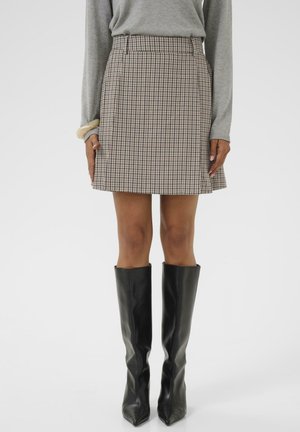 Checkered skirt in beige and brown tones, featuring a fitted waist, A-line silhouette, and knee-length hem. Worn with tall black boots.