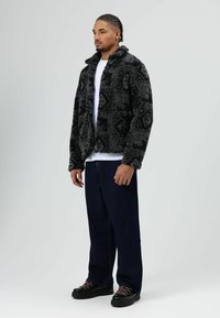 Zwart- en grijsgevlekt imitation bontjack met een kraag, gedragen over een wit T-shirt. Gecombineerd met donkere spijkerbroek en zwarte schoenen.