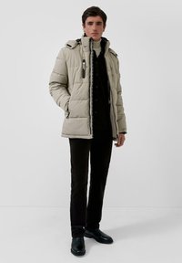 Šviesiai rudas paminkštintas švarkas su užtrauktuku priekyje, gobtuvu ir juodais akcentais. Dėvimas virš tamsios palaidinės ir juodų kelnių, su juodais batais.