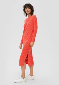 Koralewe sweter z fakturą dzianinową i spódnica w zestawie z wzorem w chevron, z bocznym rozcięciem. Połączone z białymi sneakersami dla kontrastu.