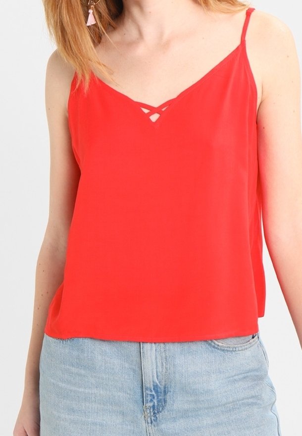 Haut rouge sans manches avec bretelles ajustables, présentant un décolleté en V et un détail découpé. Tissu lisse, coupe ample, associé à du denim.