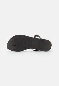 Black sandal with a textured sole. Features slender straps and a small metal accent. Rubber outsole with grip patterns and circular studs.