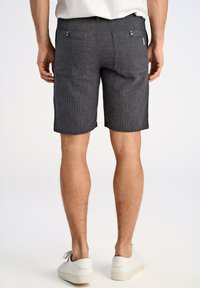 Grijs gestreepte korte herenbroek met twee achterzakken, knoopsluitingen en een getailleerde fit, gecombineerd met witte sneakers.