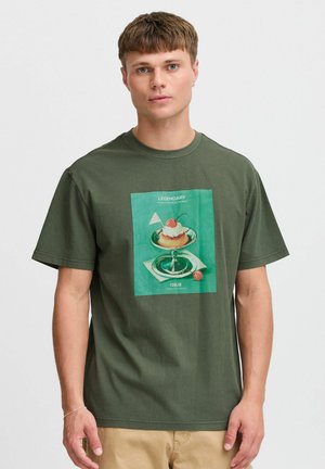 Maslinasto zelena pamučna majica s kratkim rukavima koja prikazuje centralno grafičko ilustraciju desertnog jela, s natpisom iznad i ispod. Opušteni kroj.