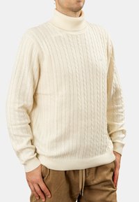 Maglione a collo alto color crema con motivo a trecce, polsini e orlo a coste. Tessuto morbido con una vestibilità ampia, caratterizzato da un piccolo logo.