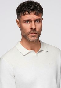 Witte lange mouwen polo met een zachte textuur, voorzien van een klassieke kraag en een subtiel geborduurd logo op de borst.