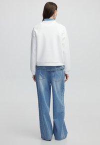 Sudadera blanca con cuello redondo, corte relajado y puños de canalé, combinada con unos vaqueros de mezclilla de pernera ancha en azul claro con bolsillos traseros.