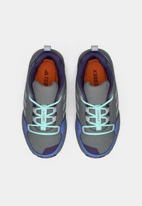 Um par de sapatilhas atléticas cinzentas e azuis com atacadores azul claro, forro interior roxo e palmilhas laranja com a marca "TERREX", vistas de cima.