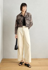 Beskåret jakke med leopardmønster, svart topp, off-white vide bukser og svarte sandaler. Aklimatisert med en liten svart håndveske.