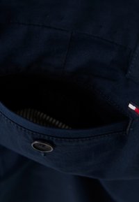 Mörkblå skjorta med en stor bröstficka, utrustad med en knappstängning och ett inre randigt foder. Mjuk tygstruktur, enkel design.