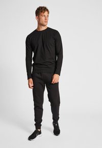 Schwarzes Langarmshirt und passende Jogginghose aus weichem Material. Die Schuhe sind schwarz mit weißen Sohlen. Schlichte und funktionale Sportbekleidung.