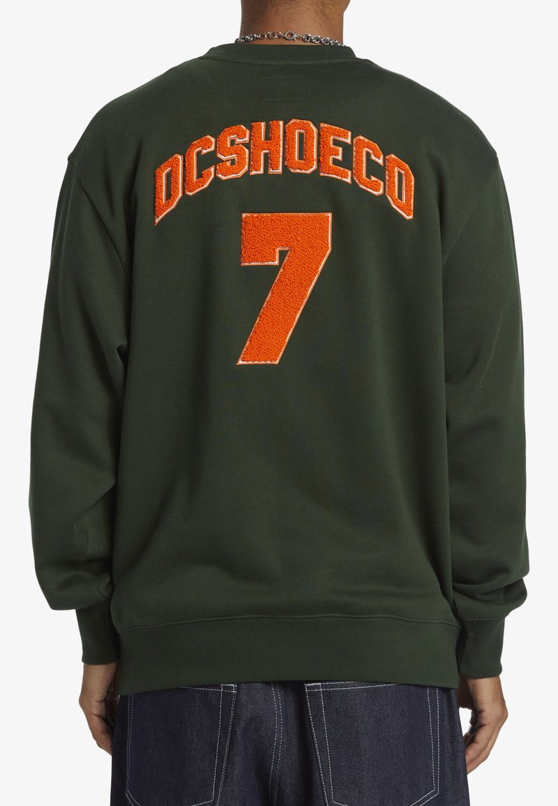 Groen sweatshirt met oranje geborduurde tekst "DCSHOECO" en het nummer "7" op de achterkant. Heeft lange mouwen en geribde manchetten.