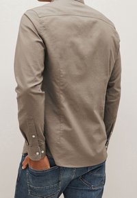 Langarmhemd in Khaki mit Kragen, Knopfmanschetten und einer glatten Textur. Kombiniert mit blauen Jeans aus Denim mit mehreren Taschen.