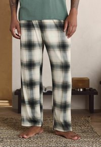 Pantalons de pyjama à carreaux en tons crème, noir et gris, présentant une coupe décontractée et un tissu doux. Avant plat avec poches latérales pour plus de confort.