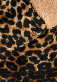 Leopard print fabric featuring black and golden-brown spots with a textured feel; includes a tan label in a corner.