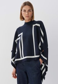 Strickponcho in Marineblau mit weißen geometrischen Mustern, leichtes Material, hoher Kragen und offene Seiten für Bewegungsfreiheit.