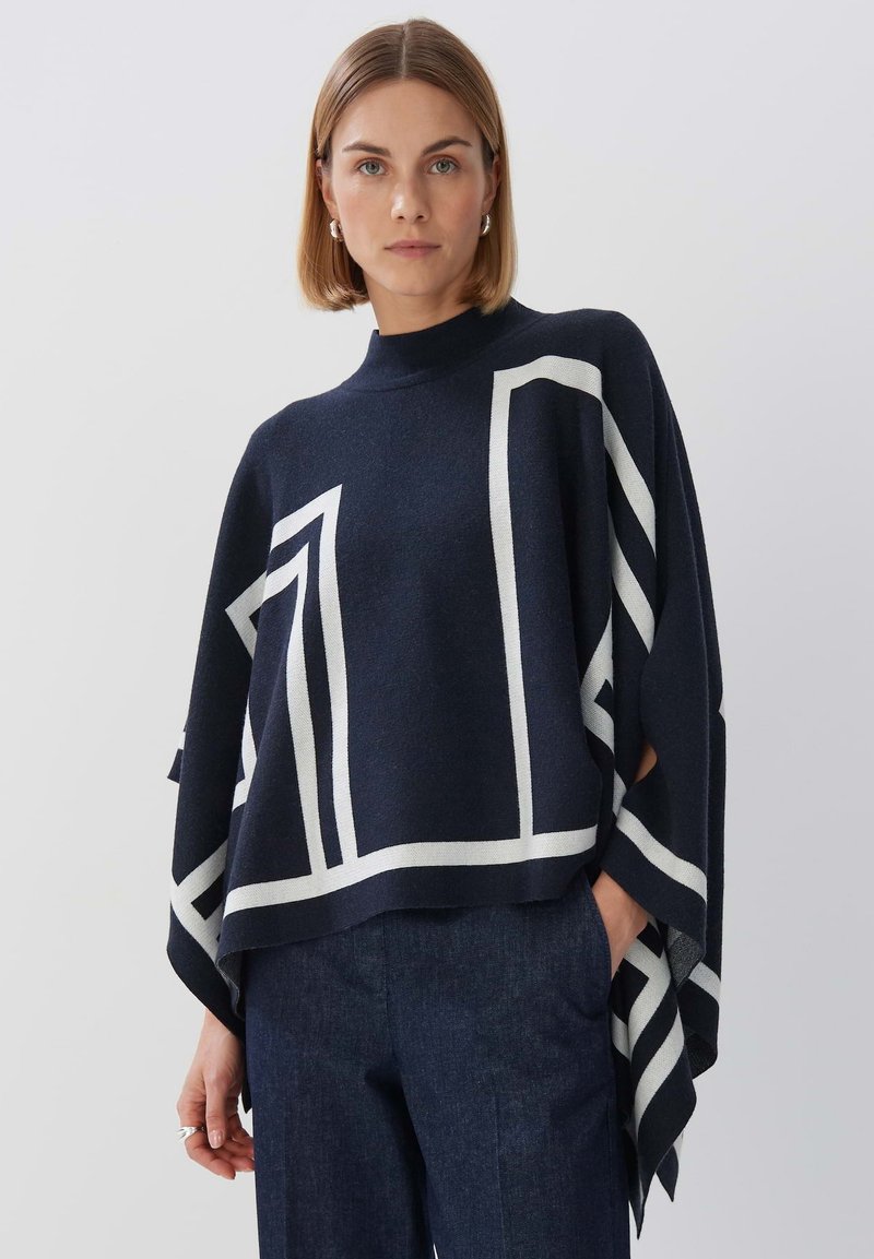 Strickponcho in Marineblau mit weißen geometrischen Mustern, leichtes Material, hoher Kragen und offene Seiten für Bewegungsfreiheit.