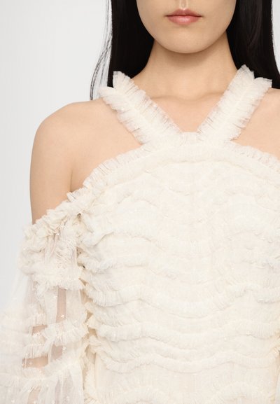 Witte ruffled top met een kruislings bandontwerp, textuurstof met gelaagde frills en doorschijnende mouwen. Detailgericht met subtiele glans.