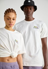 Weiße Baumwoll-T-Shirts mit kurzen Ärmeln, verziert mit buntem "On Vacation"-Stickerei. Ein Shirt ist an der Taille geknotet.