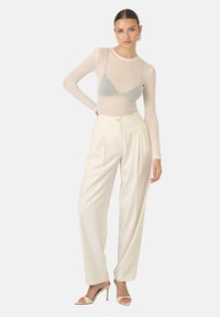 Przezroczysty top z długim rękawem, okrągłym dekoltem i jasnoszarym trójkątnym biustonoszem, w połączeniu z białymi spodniami o szerokich nogawkach i wysokim stanem.
