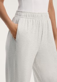 Svetlo sivi trenirki narejeni iz mehkega blaga, z elastičnim pasom in stranskimi žepi, z gladko teksturo in subtilnim vzorcem.